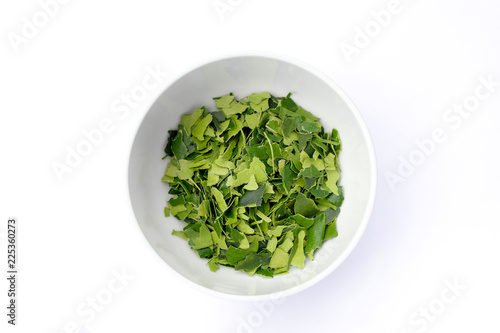Kaffir lime leaves in a white bowl top view isolated on white background. © Sunisa