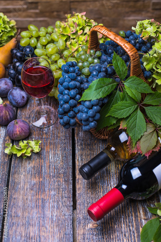 Autumn harvest of ripe grape, plums, figs and two bottle of wine on a wooden table.