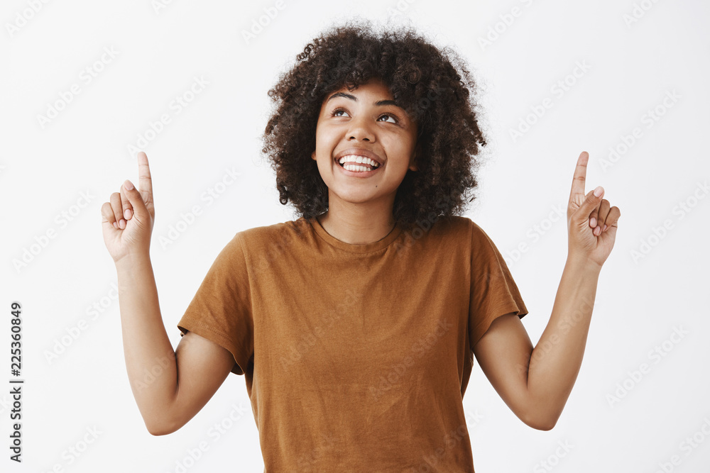 Girl happily looking at sky enjoying nice summer weather. Portrait of attractive dreamy african american female student in brown t-shirt with afro hairstyle looking and pointing up with joyful smile Girl happily looking at sky enjoying nice summer weather. Portrait of attractive dreamy african american female student in brown t-shirt with afro hairstyle looking and pointing up with joyful smile