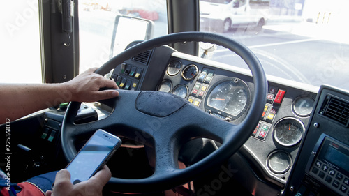 Closeup photo of truck driver typing on smartphone while driving. Danger in transport. Irresponsible driver