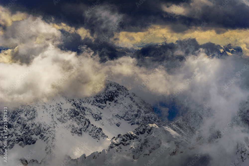 Schneebedeckte Berge umgeben von vorbeiziehenden dramatischen Wolken.

