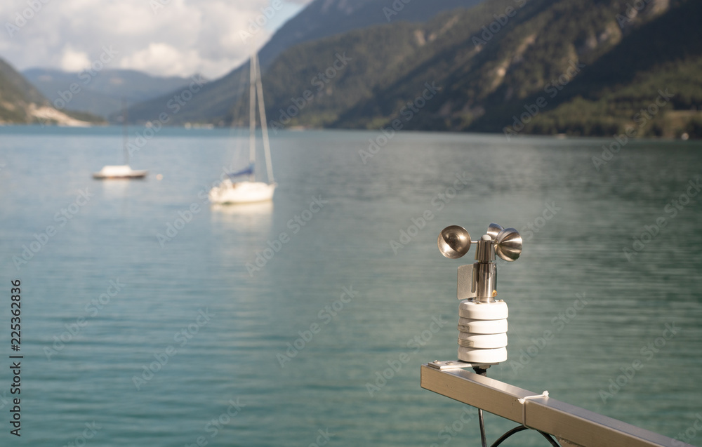 Windmesser mit Segelbooten auf einem See im Hintergrund