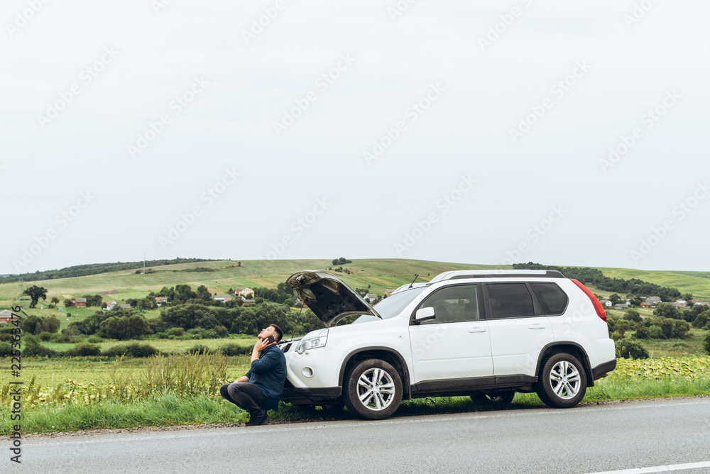 man sitting near broken car with phone, looking for help man sitting near broken car with phone, looking for help