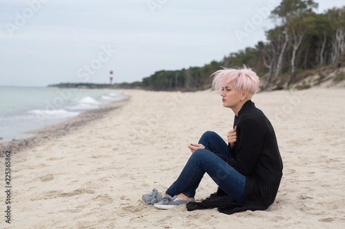 beautiful lonely sad girl hipster with a stylish hairstyle and pink hair smokes and looks at the sea