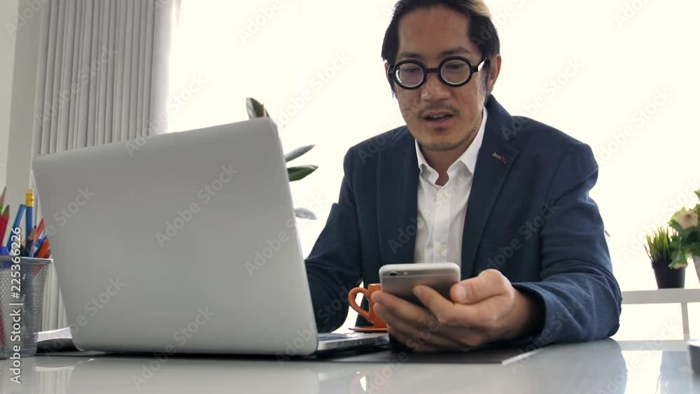 Business man in office using laptop and cell phone, 4K Slow motion of office man talking and typing on mobile phone . Business man in office using laptop and cell phone, 4K Slow motion of office man talking and typing on mobile phone .