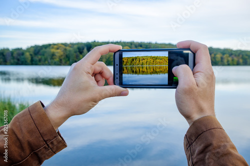 Men's hands hold the phone and take pictures of the autumn landscape on the lake