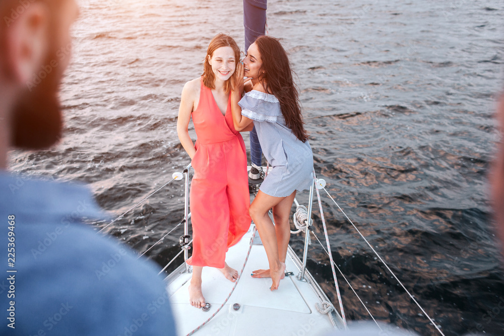 Beautiful young women stand together and pose. They wispering and laughing. Men stands adn look at them. Women are on bow of yacht. Beautiful young women stand together and pose. They wispering and laughing. Men stands adn look at them. Women are on bow of yacht.
