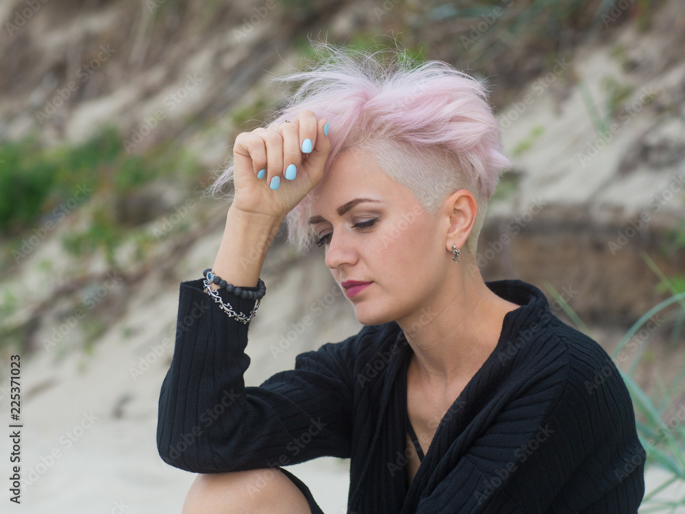 Portrait of a beautiful worried sad girl /young woman with pink hair and trendy hairstyle sitting on the beach.