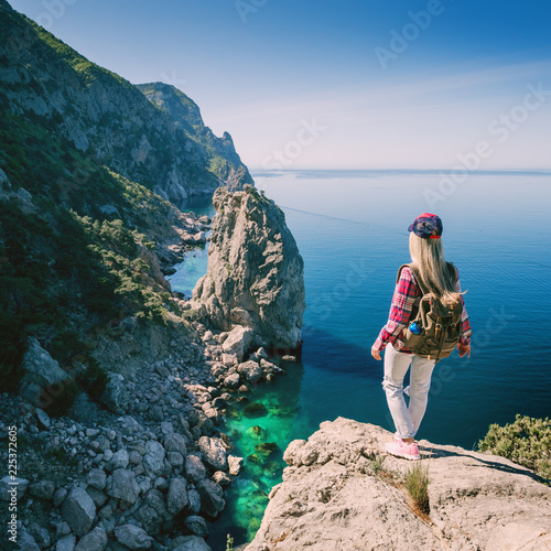 Young woman backpacker in the mountains by the sea on the island enjoys the sea view. Hipster girl with backpack hiking tourist traveler.
