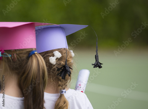 horizontal image with detail of two little girls photographed from behind with the graduation hats at the kindergarten party