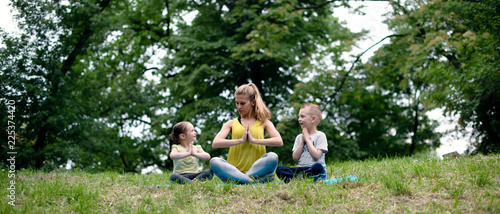 Fototapeta Naklejka Na Ścianę i Meble -  Young family of mother and children son and daughter are engaged in fitness, yoga, exercise in the park. Healthy sport lifestyle concept