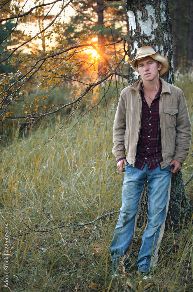 young man in cowboy suit in autumn forest at sunset