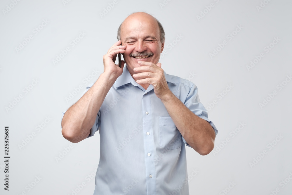 Happy mature man bald and with mustache talking on mobile, isolated on white background. he is laughing because his son told him great news Happy mature man bald and with mustache talking on mobile, isolated on white background. he is laughing because his son told him great news