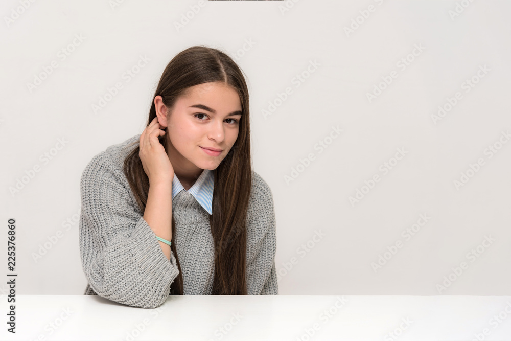 Portrait of a beautiful teenage girl on a white background with different emotions sitting at a table. Portrait of a beautiful teenage girl on a white background with different emotions sitting at a table.