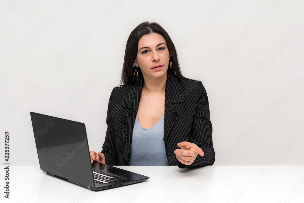 Portrait of a beautiful brunette woman on a white background with different emotions sitting at a table with a laptop. Portrait of a beautiful brunette woman on a white background with different emotions sitting at a table with a laptop.