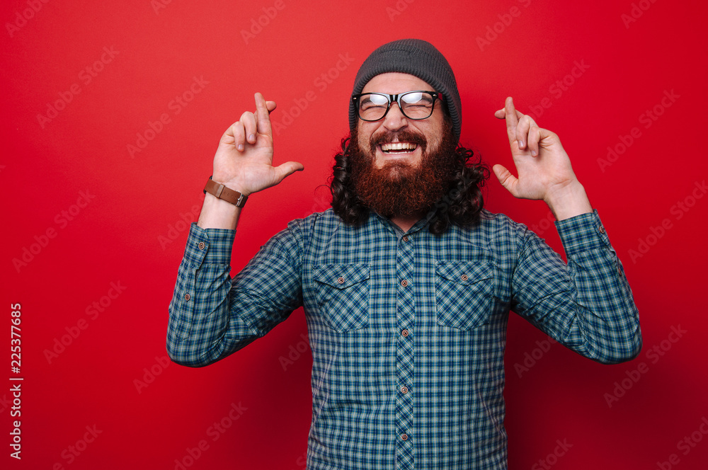 Naklejka premium Portrait of bearded man with crossed fingers over red background