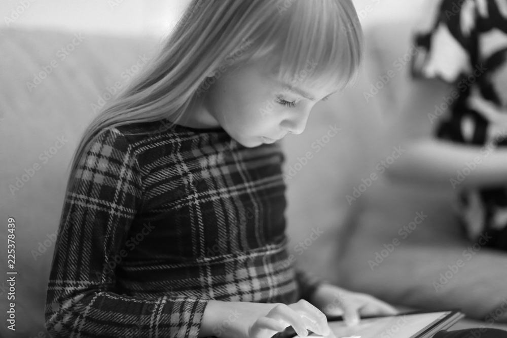 A girl is sitting on the sofa in the room and playing a computer game on a tablet A girl is sitting on the sofa in the room and playing a computer game on a tablet