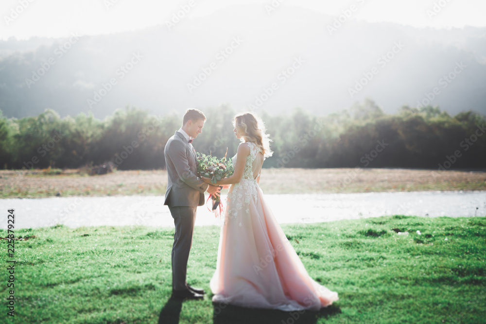 Elegant stylish happy brunette bride and gorgeous groom on the background of a beautiful river in the mountains