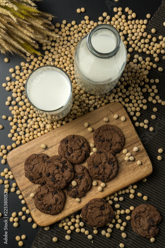 top view of the chocolate chip cookies on the wooden tray, a glass of soy milk, a pile of soybeans, a bottle of soy milk with dried wheat bouquet and the napery. © Krisada