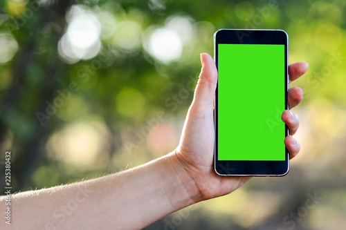 Close up of a woman using mobile smart phone outdoor. Green screen for uploading videos. Cropped image of woman's hands holding smart phone with blank copy space screen for your text message.