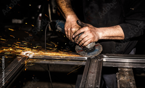 Craftsman sawing metal with disk grinder in workshop. Grinding metal with sparks flying.