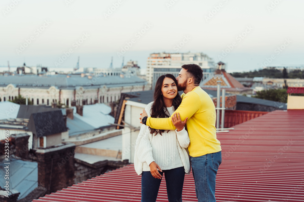 Loving young couple is standing on the roof of the house.
