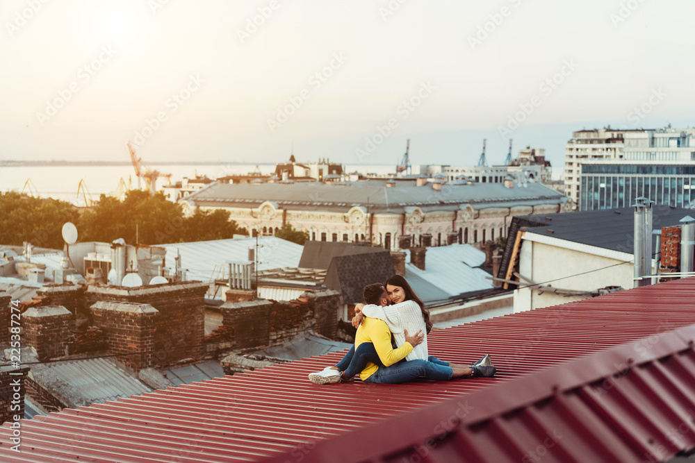 Loving young couple is sitting on the roof of the house.