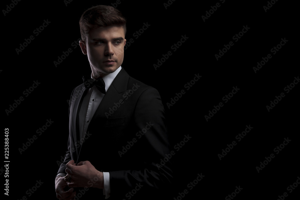 elegant man buttons his black tuxedo and looks to side elegant man buttons his black tuxedo and looks to side
