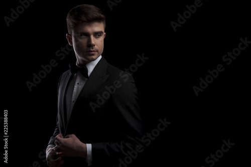 elegant man buttons his black tuxedo and looks to side