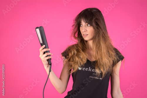 Woman with a hair curler. Girl with disheveled hair on a pink background. Creative concept on the problem of styling