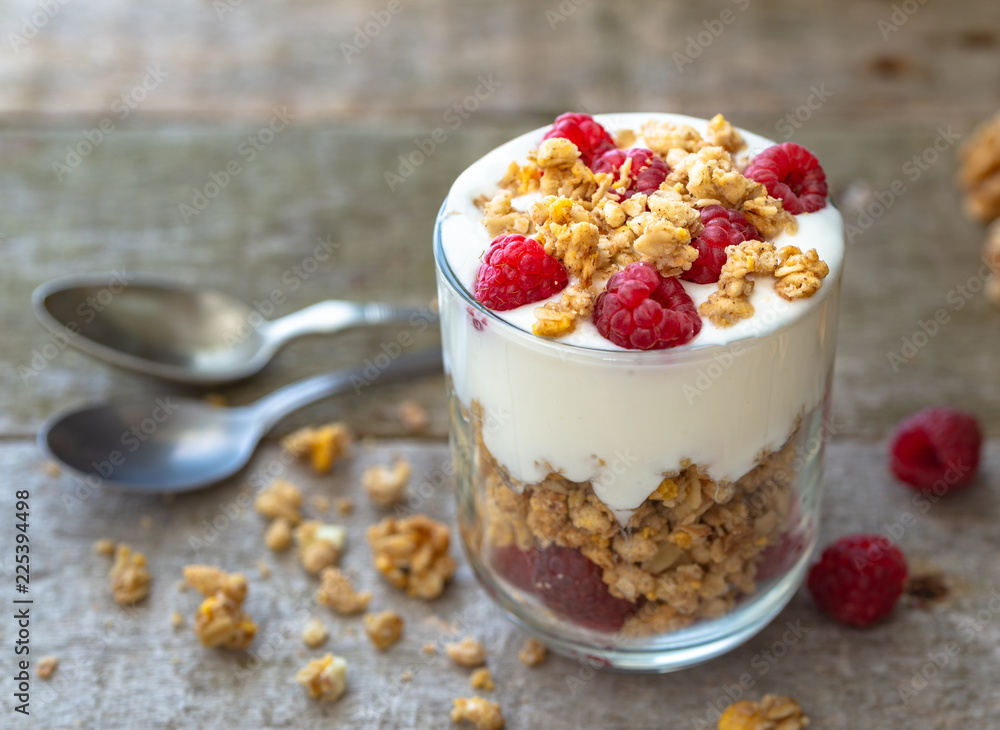 White yogurt with muesli in glass bowl with pieces raspberries on top on natural wooden desk. White yogurt with muesli in glass bowl with pieces raspberries on top on natural wooden desk.