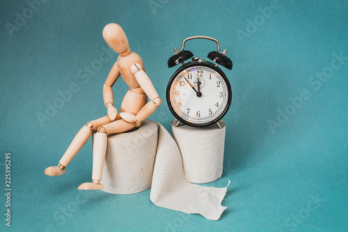 Wooden figure sit on a roll of toilet paper near alarm clock. Concept of the problem with digestion. photo