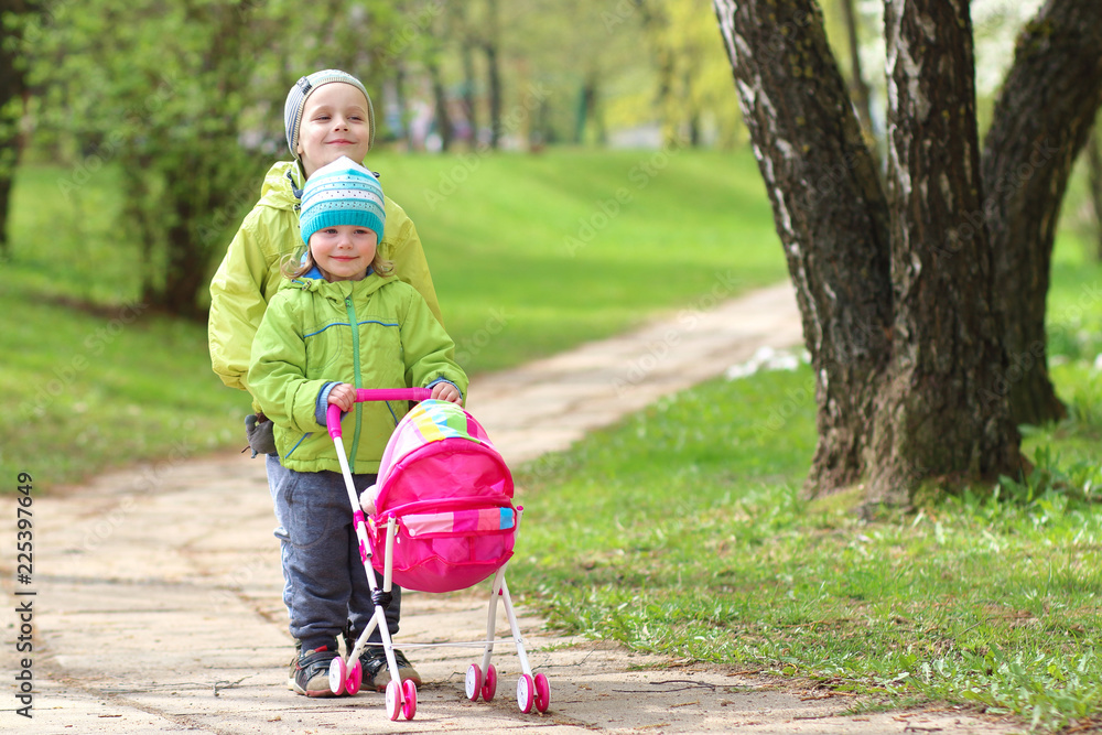 © dzmitrock87 - children's friendship. Small friends. Children walk in green park. Little boy and girl with toy carriage for doll. Brother and sister are together