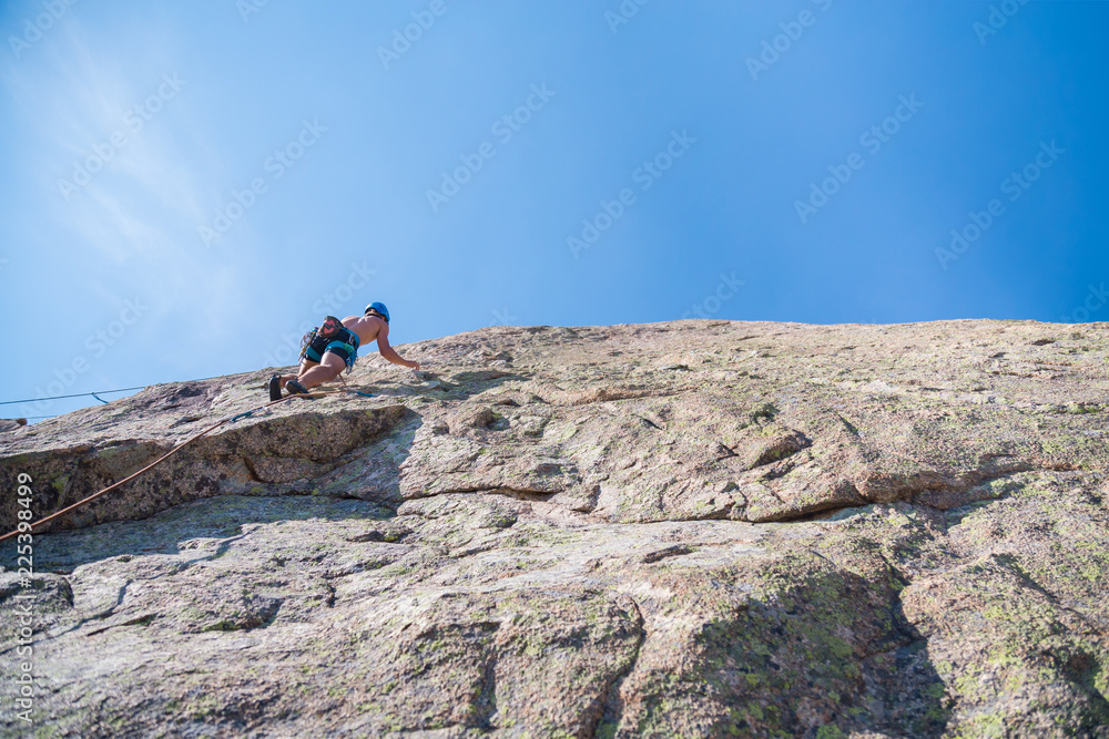 From below shot of shirtless male climber climbing mountain wall on amazing sunny day 