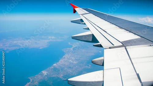 View from the window of airplane wing above sea and land on bright sunny day