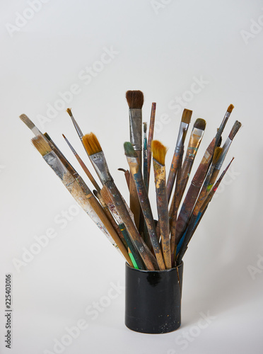 Various dirty paint brushes in a black cup isolated on white background with copy space, close-up. Colorful paintbrushes and artistic Paint Tools 