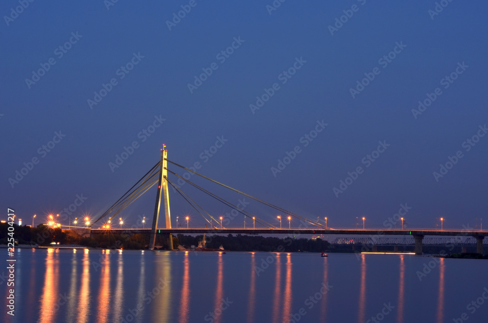 Bridge at night beside the Dnipro river with reflection in water