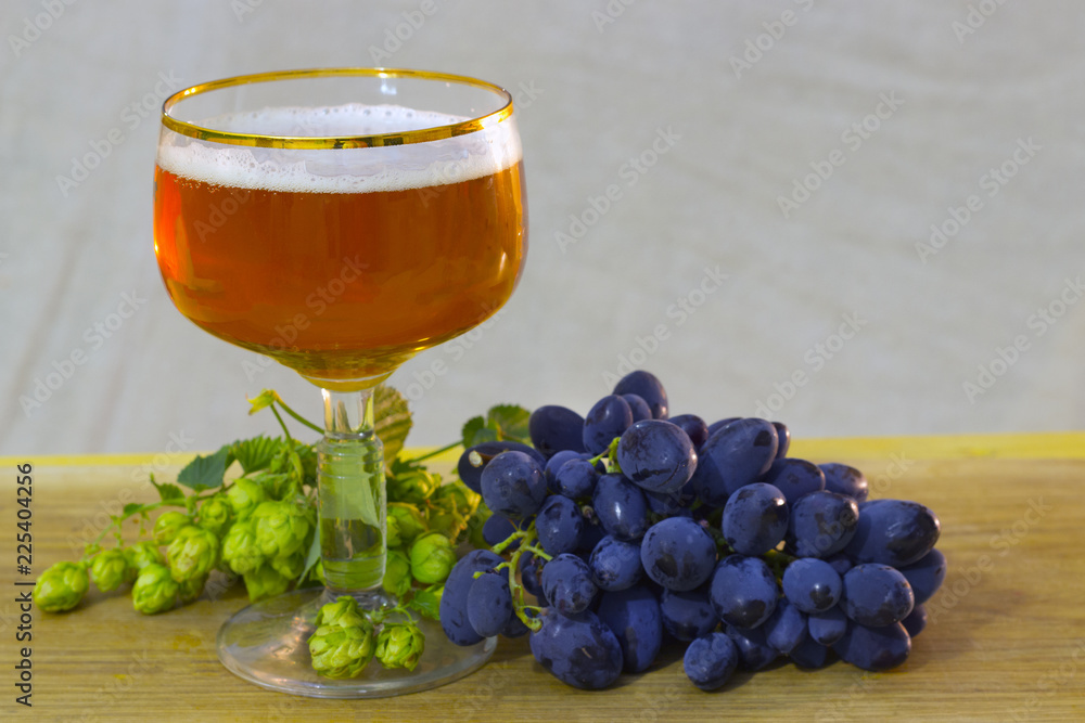a beautiful glass of warm beer with a bunch of grapes and fresh hops a beautiful glass of warm beer with a bunch of grapes and fresh hops