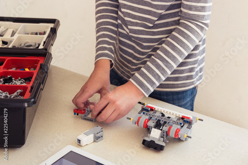 A boy teenager at a school of robotics collects a robot from plastic parts and programs it on a tablet. Museum of Science and Robotics. STEM education for children. Free space for text.