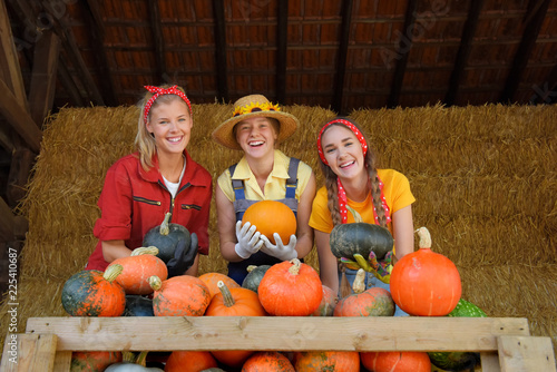 Three girls smile happily together showing off  their harvested pumpkins from the pumpkin  patch.