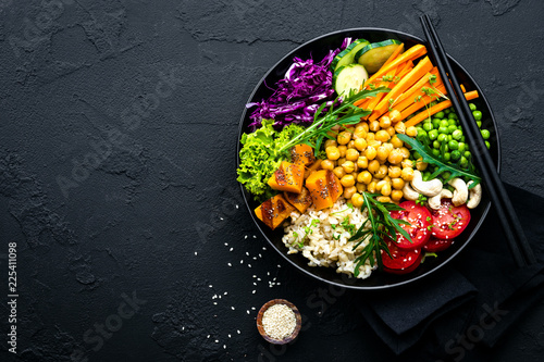 Bowl dish with brown rice, cucumber, tomato, green peas, red cabbage, chickpea, fresh lettuce salad and cashew nuts. Healthy balanced eating photo