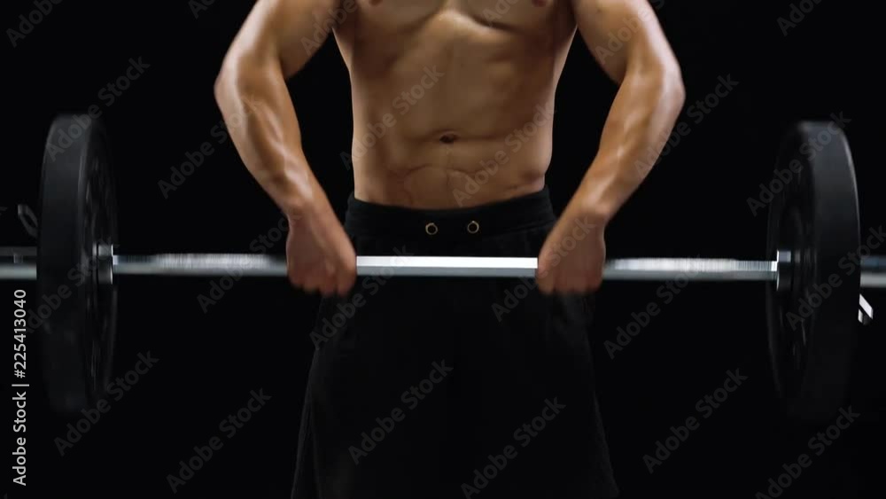 Man is doing exercises with a barbell, training on a black background in the studio Man is doing exercises with a barbell, training on a black background in the studio