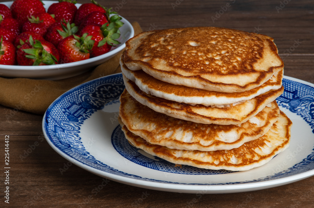 Plain stack of pancakes on a blue and white plate with a bowl of fresh strawberries in the background.