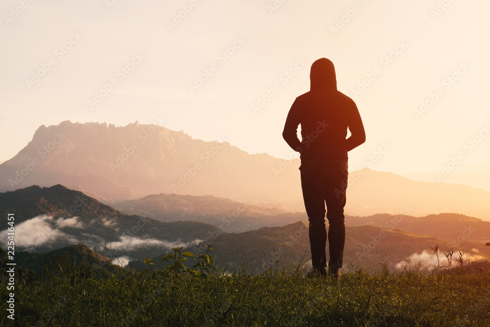 Man silhouette view from behind standing looking far away at Mount Kinabalu on sunrise.