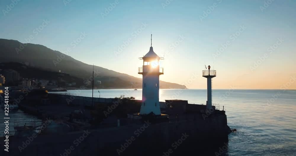 Lighthouse for ships and sunrise over the sea. Epic on the edge of the mountain valley. Sun flare. 4k drone flight. Aerial establisher. City by the ocean. Concept of marine travel. Film vintage colors Lighthouse for ships and sunrise over the sea. Epic on the edge of the mountain valley. Sun flare. 4k drone flight. Aerial establisher. City by the ocean. Concept of marine travel. Film vintage colors