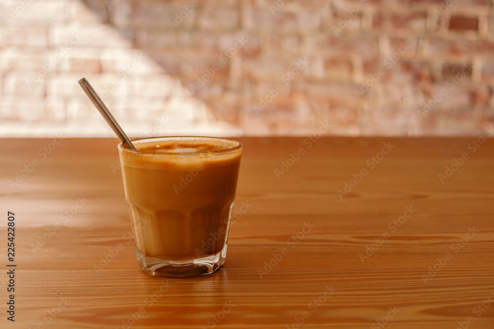 Flat white coffee in transparent glass on table in cafe. It is espresso-based coffee drink consisting of espresso with microfoam steamed milk with fine bubbles with a glossy or velvety consistency Flat white coffee in transparent glass on table in cafe. It is espresso-based coffee drink consisting of espresso with microfoam steamed milk with fine bubbles with a glossy or velvety consistency