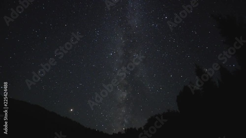 Milky Way time lapse, rotation in dark sky over Kyrgyz mountains with black tree sihouettes photo