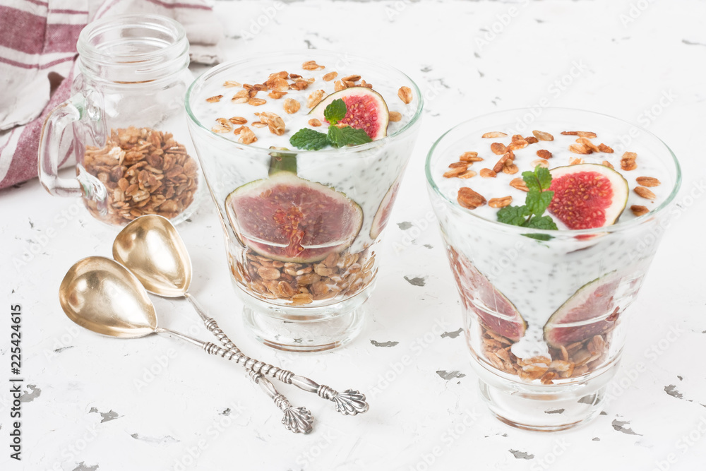 Chia seeds pudding parfait / Chia seeds pudding parfait with yogurt, figs, oatmeal granola, and mint in glass on white background