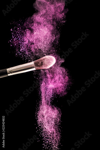 Make up brush with purple dust powder explosion isolated on black background. Beauty and fashion concept. Close up, selective focus