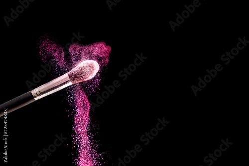 Make up brush with purple powder dust explosion isolated on black background. Space for text and design. Close up, selective focus